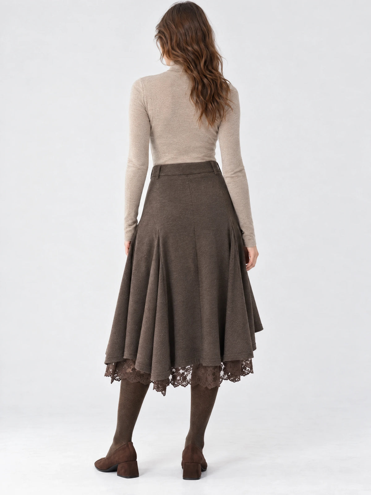 Rear studio view of a model wearing a Brown cotton asymmetric hem midi skirt with a fitted waistband, flowing panels, and lace-trimmed hem.