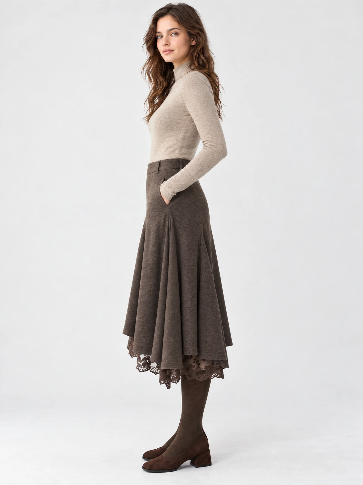 Side studio view of a model wearing a Brown asymmetric hem midi skirt with a flared silhouette, lace-trimmed hem, and hand in pocket.