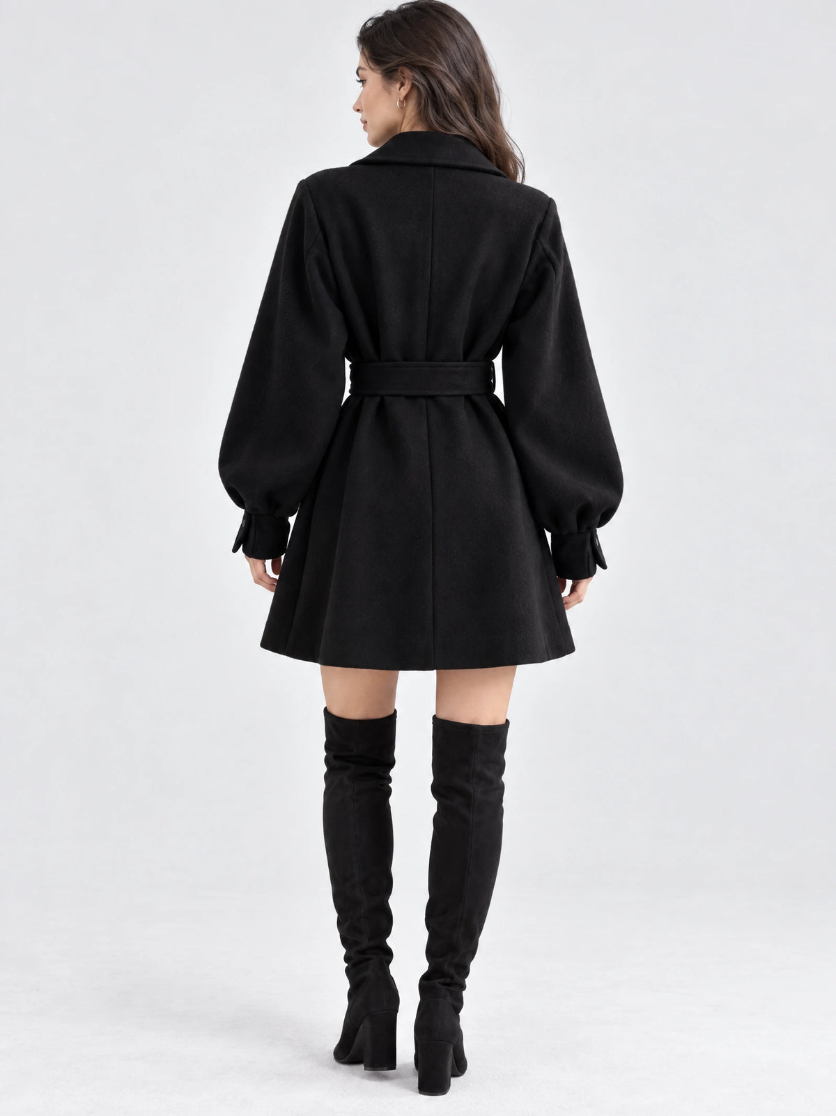 Rear studio view of a model wearing a Black belted lantern sleeve wool coat with a flared skirt and center back seam.