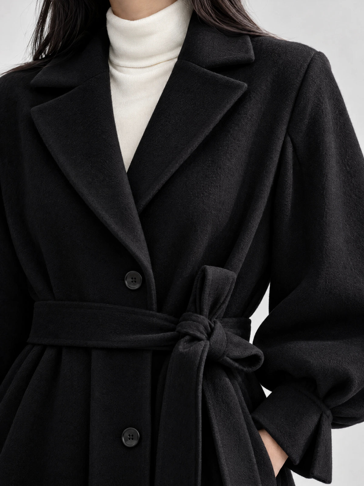 Close-up of the Black belted lantern sleeve wool coat with notched lapels, button front, and tied waist belt.