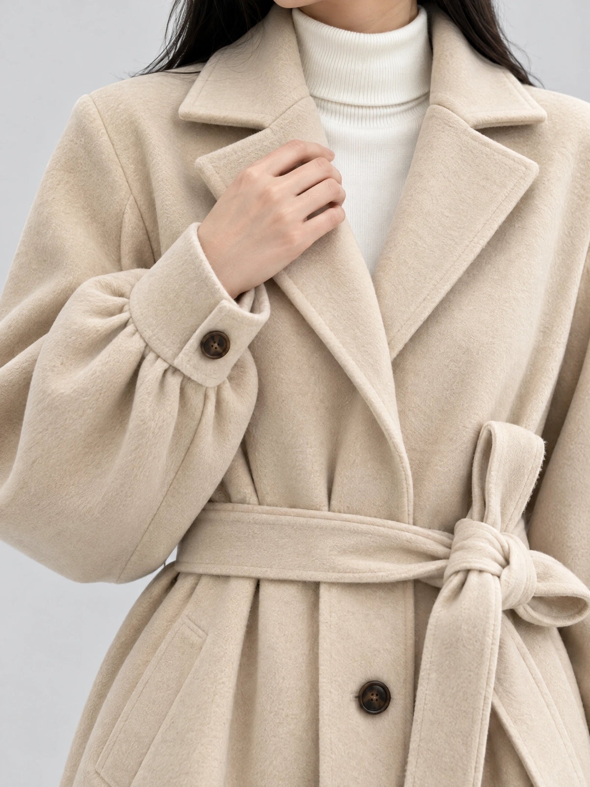 Close-up of the Beige belted lantern sleeve wool coat, showing its wide lapels, buttoned cuff, soft fabric texture, and tied waist belt.