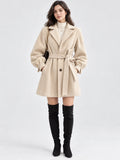 Front studio view of a model wearing a Beige belted lantern sleeve wool coat with wide lapels and cuff ties.