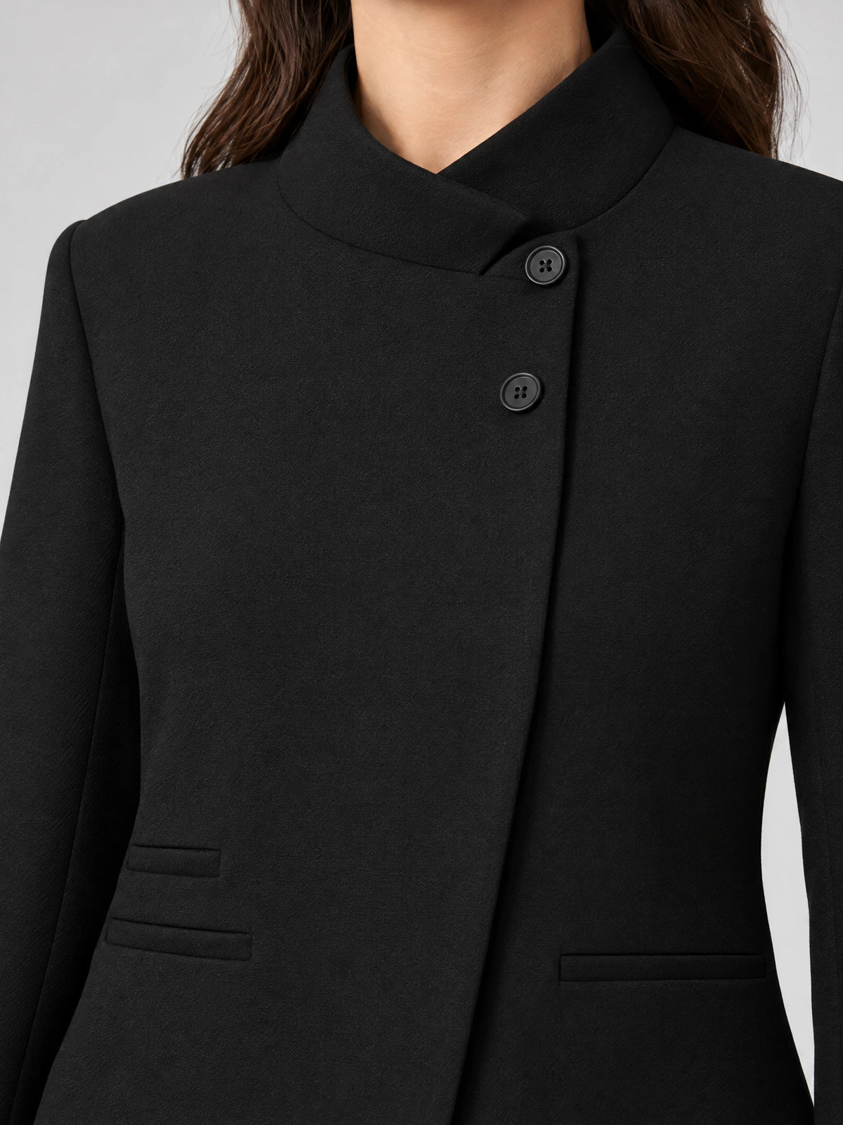 Close-up of the Black Blazer Blouse showing its stand collar, asymmetric button closure, and welt pockets.