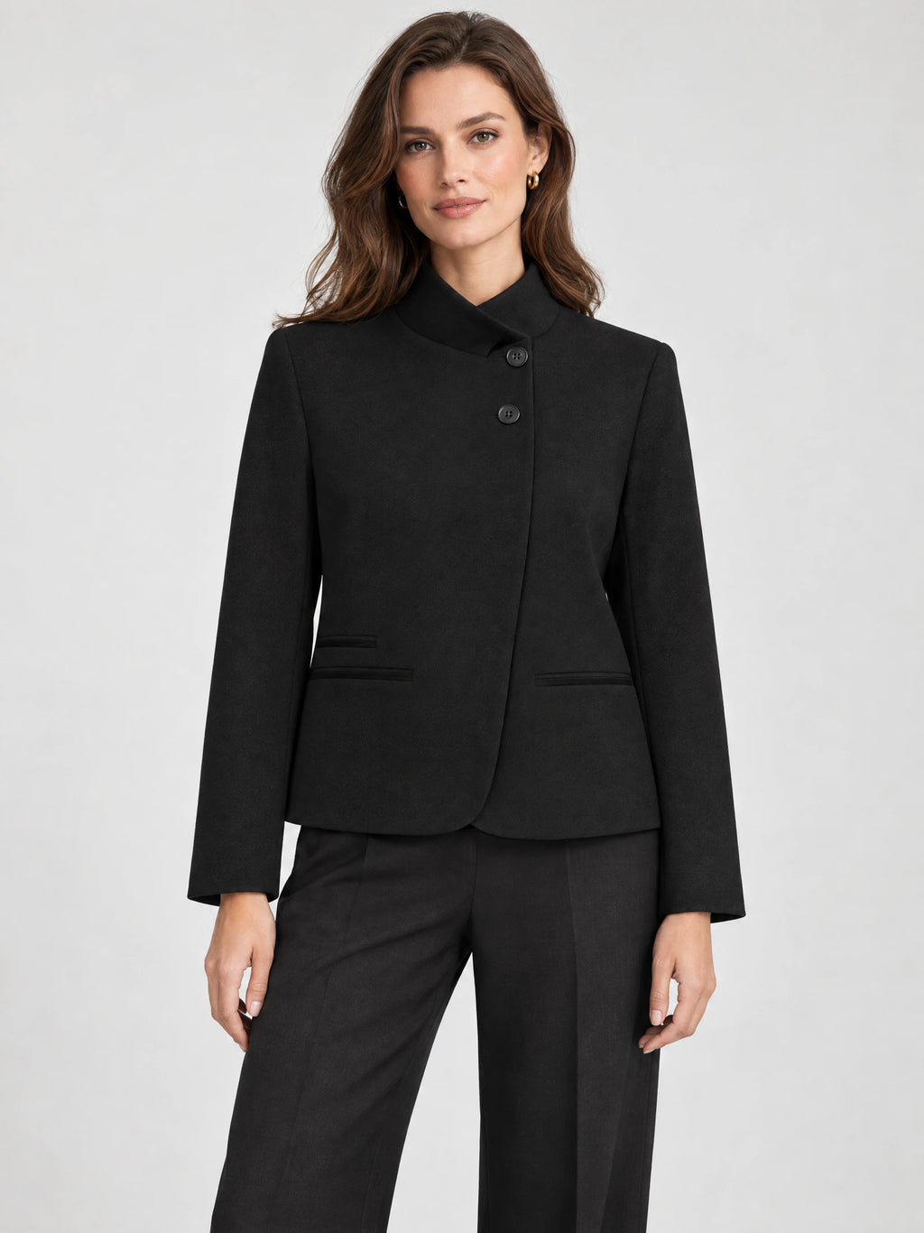 Front studio view of a model wearing a Black Blazer Blouse with an asymmetric high collar, button closure, and welt pockets.