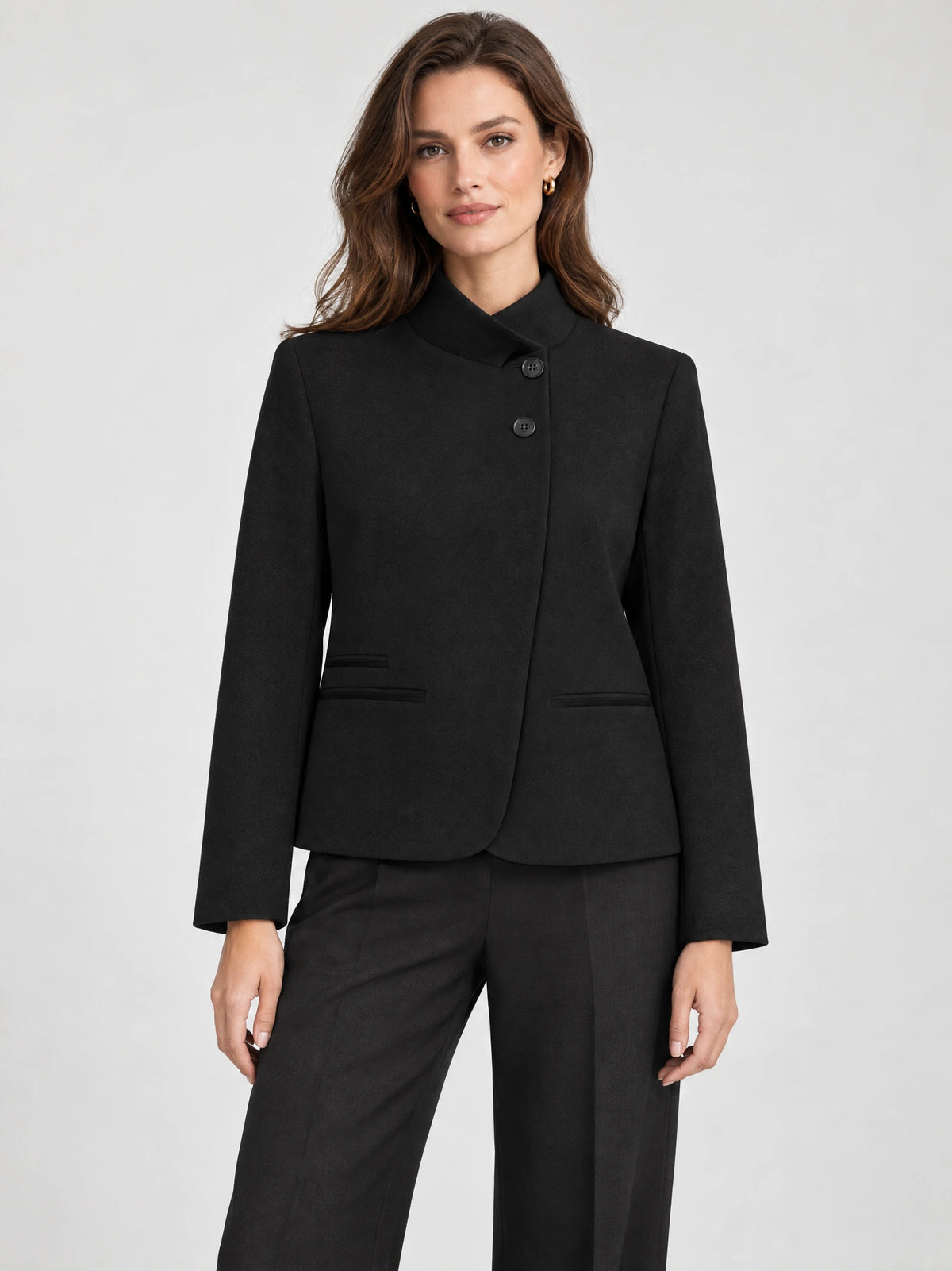 Front studio view of a model wearing a Black Blazer Blouse with an asymmetric high collar, button closure, and welt pockets.