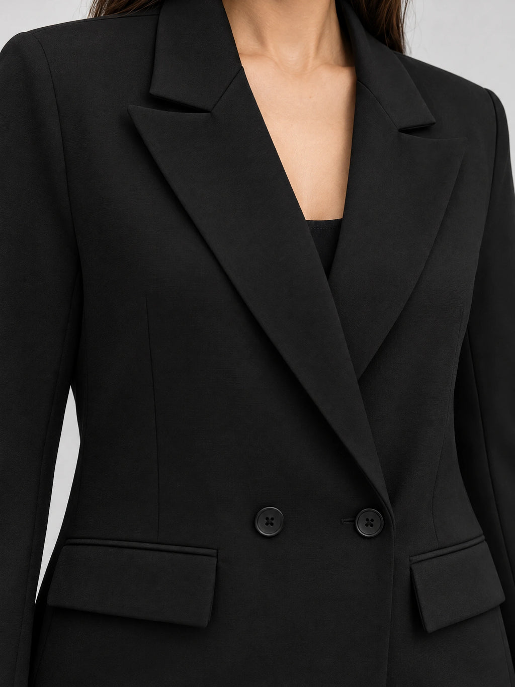Close-up of a Black double breasted blazer showing notched lapels, four-hole buttons, and flap pockets.