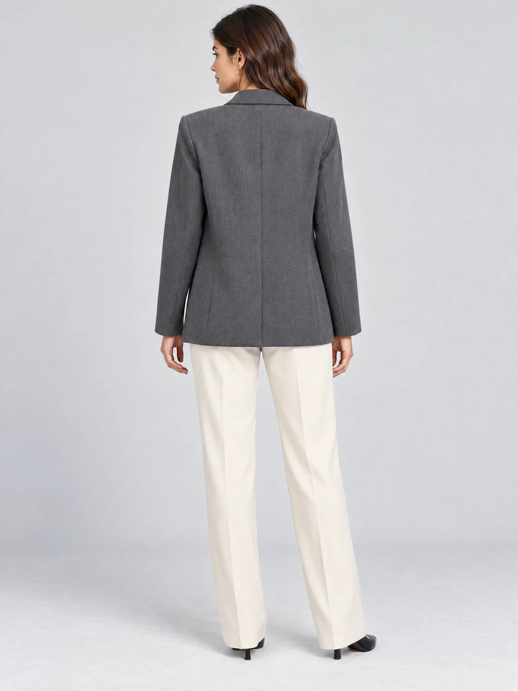 Rear studio view of a model wearing a Gray double breasted blazer with long sleeves and a tailored back seam.