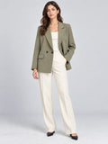 Front studio view of a model wearing a Green double breasted blazer with notched lapels and flap pockets.