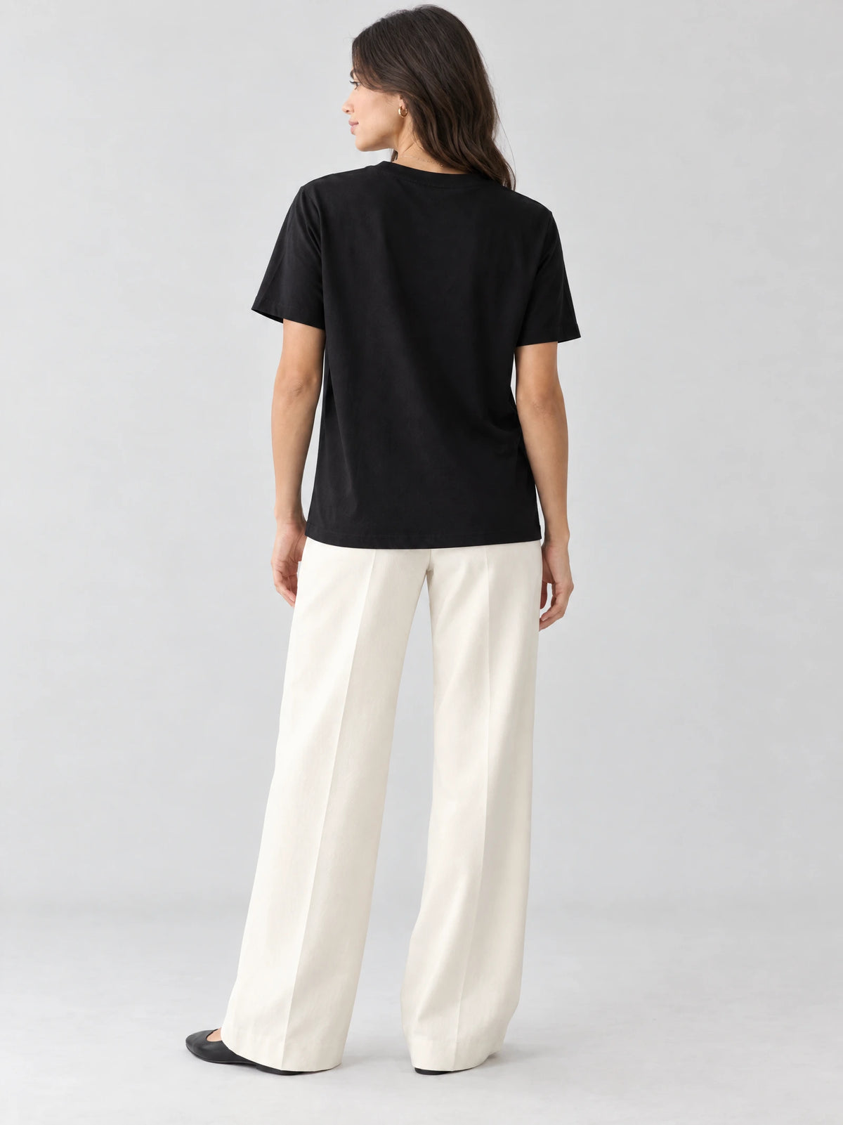 Back view of a model wearing a Black heavyweight cotton women's T-shirt in a studio.