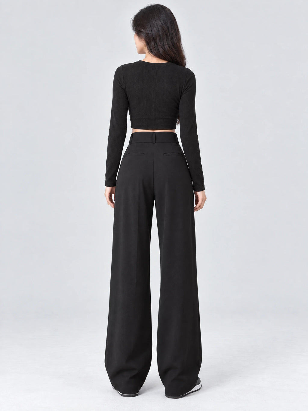 Rear studio view of a model wearing Black high waist wide leg pants with welt back pockets and a flowing full-length silhouette.