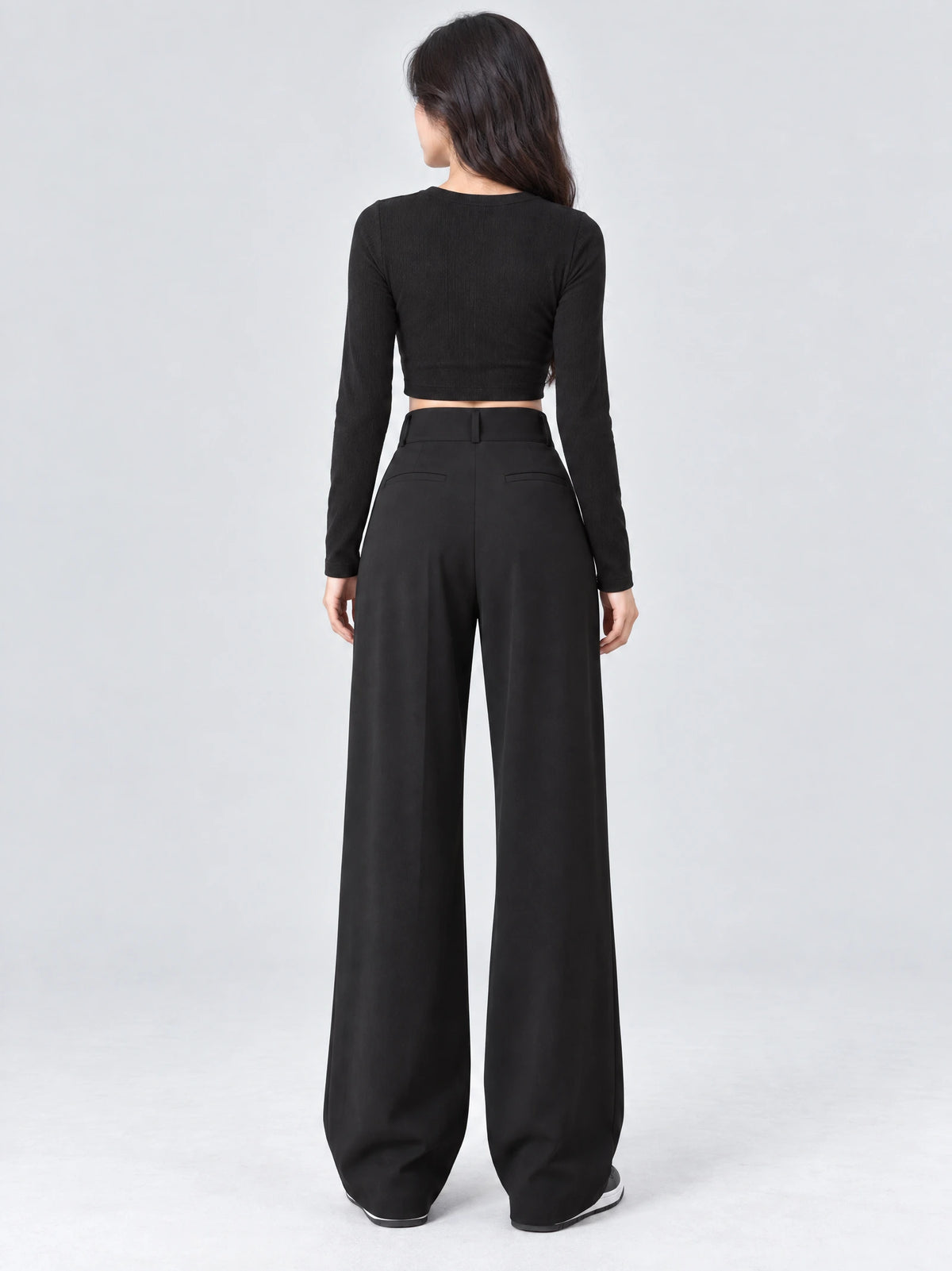 Rear studio view of a model wearing Black high waist wide leg pants with welt back pockets and a flowing full-length silhouette.