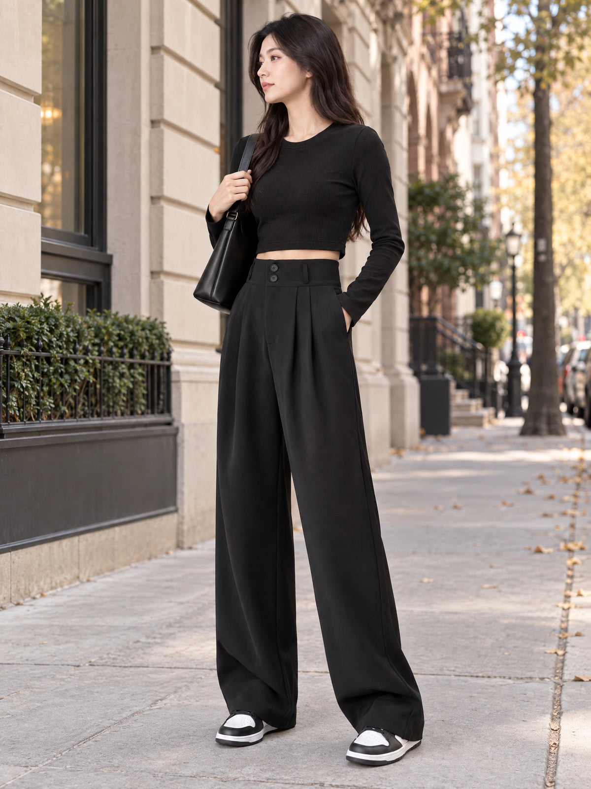 Model wearing Black high waist wide leg pants with a buttoned waistband and front pleats on a city sidewalk.