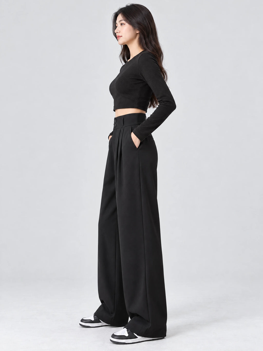 Side studio view of Black high waist wide leg pants with a buttoned waistband, pleated front, and side pockets.