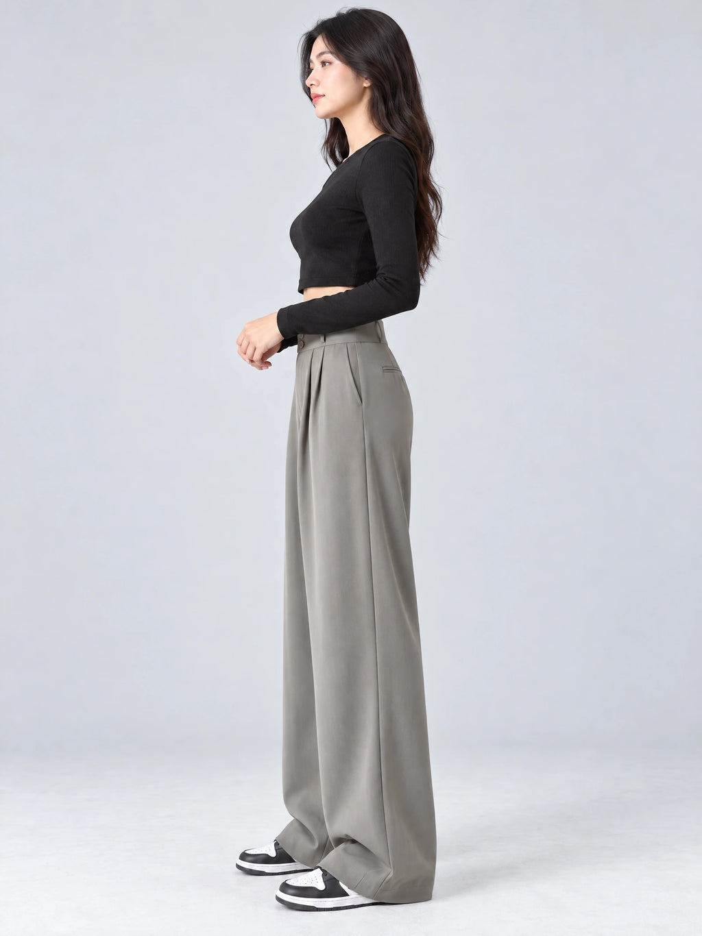Side studio view of a model wearing Gray high waist wide leg pants with front pleats and a back welt pocket.