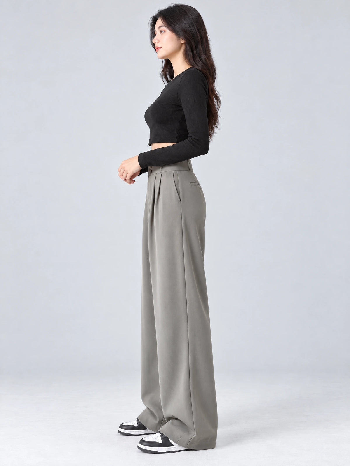 Side studio view of a model wearing Gray high waist wide leg pants with front pleats and a back welt pocket.