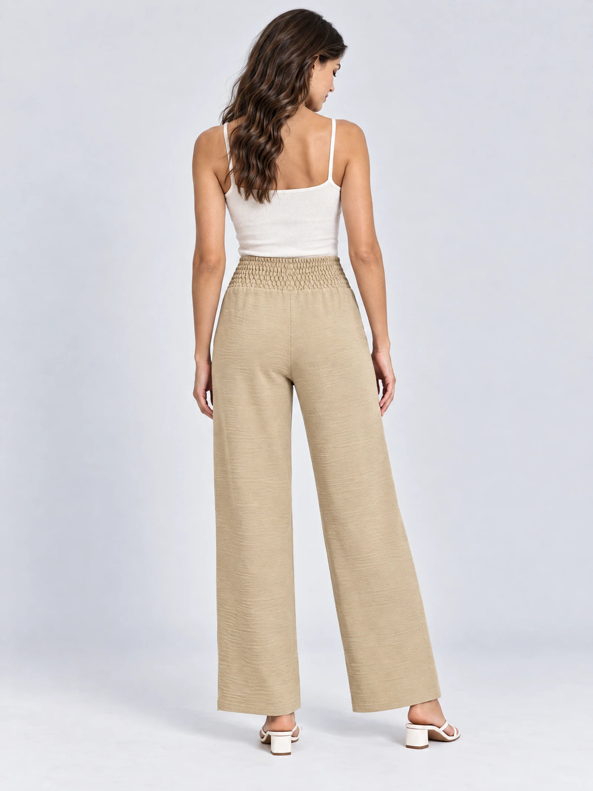 Rear studio view of a model wearing Khaki high waist wide leg pants with a smocked waistband.