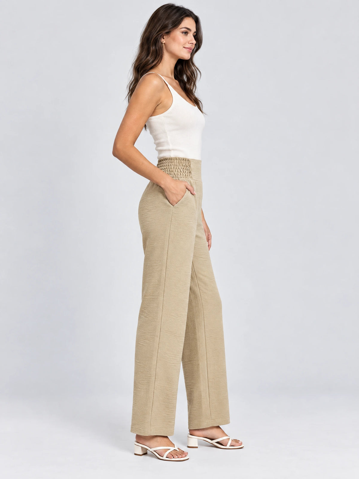 Side studio view of a model wearing Khaki high waist wide leg pants with a smocked waistband and side pocket.