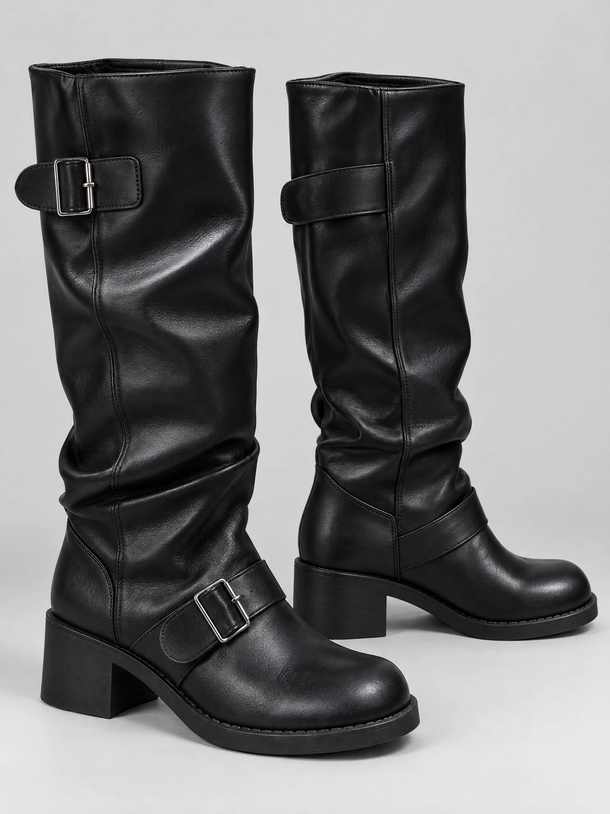 Black leather knee-high chunky boots shown in a studio pair view with buckled straps, rounded toes, and block heels.