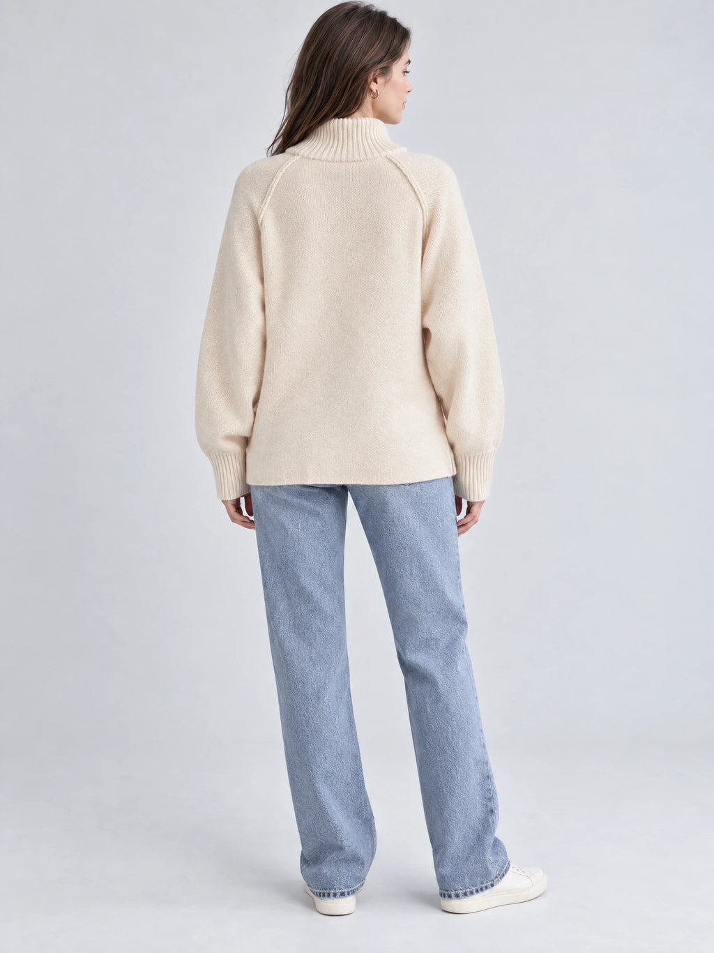 Back view of a model wearing a Beige knit full zip sweater with a ribbed high collar, raglan sleeves, and ribbed cuffs.