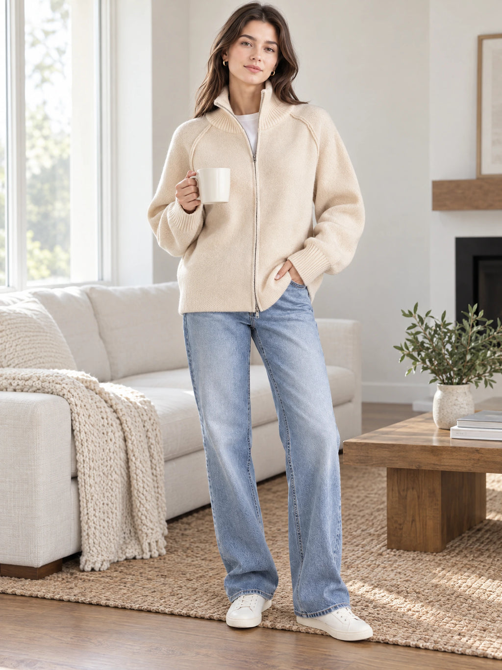 Model wearing a Beige knit full zip sweater with a ribbed stand collar while holding a mug in a sunlit living room.
