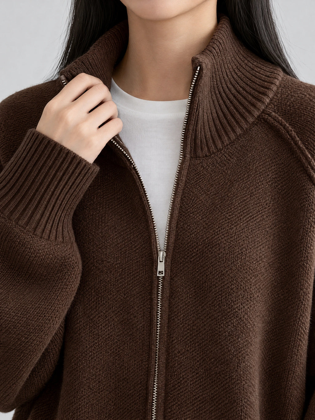 Close-up of a Brown knit full zip sweater with a ribbed stand collar, metal zipper, and ribbed cuff.
