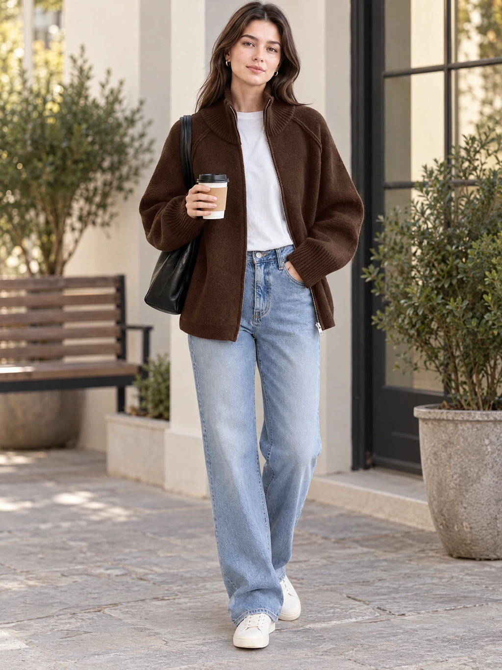 Model walks outside in a Brown Knit Full Zip Sweater with a ribbed high collar and cuffs, holding a takeaway coffee.