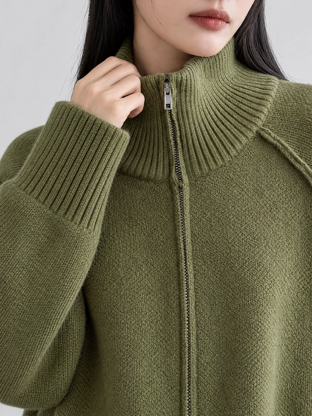 Close-up of a Green knit full zip sweater showing the ribbed high collar, zipper, and ribbed cuff.