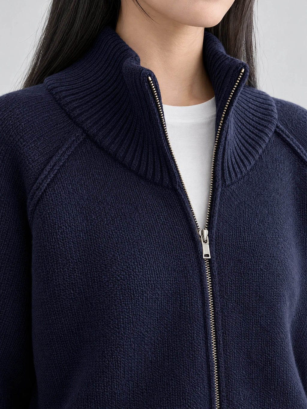 Close-up of a Navy knit full zip sweater with a ribbed stand collar and silver zipper.