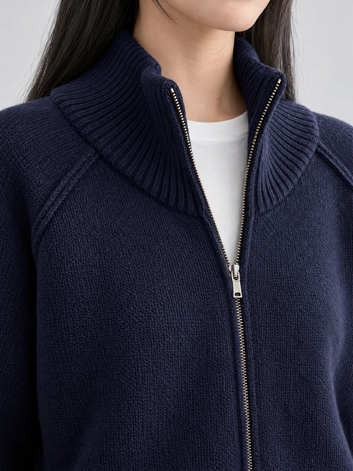 Close-up of a Navy knit full zip sweater with a ribbed stand collar and silver zipper.