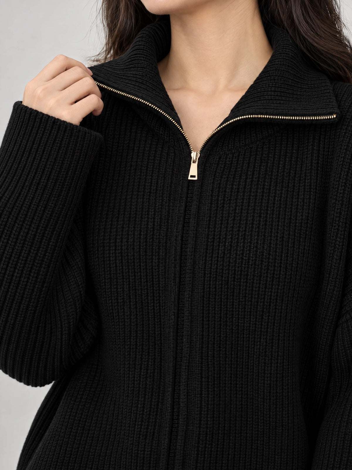 Close-up of a Black knit turtle neck cardigan with ribbed texture, a wide folded collar, and a gold-tone front zipper.