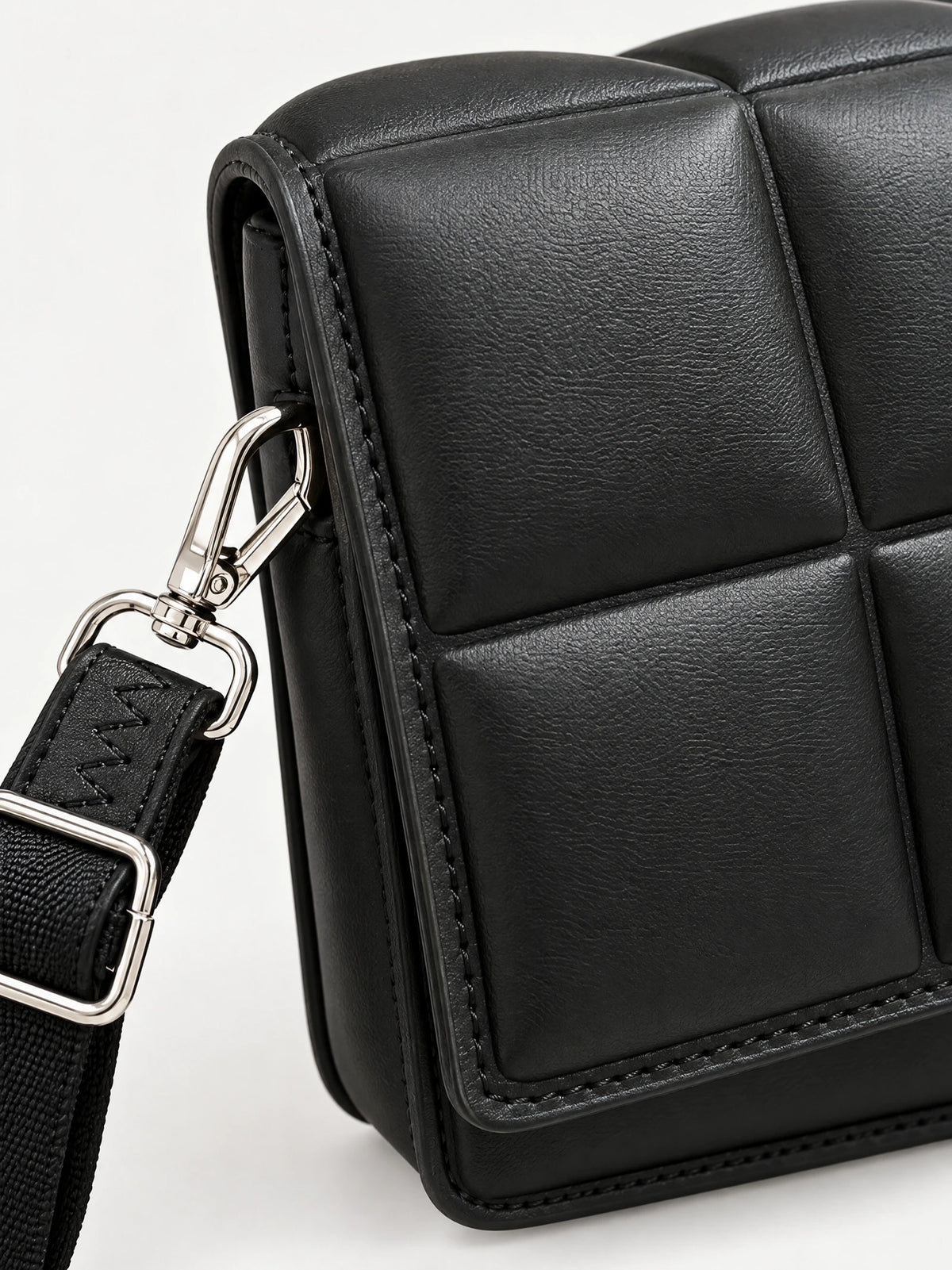 Close-up of a Black leather cross body bag showing textured panel stitching and a strap clasp.