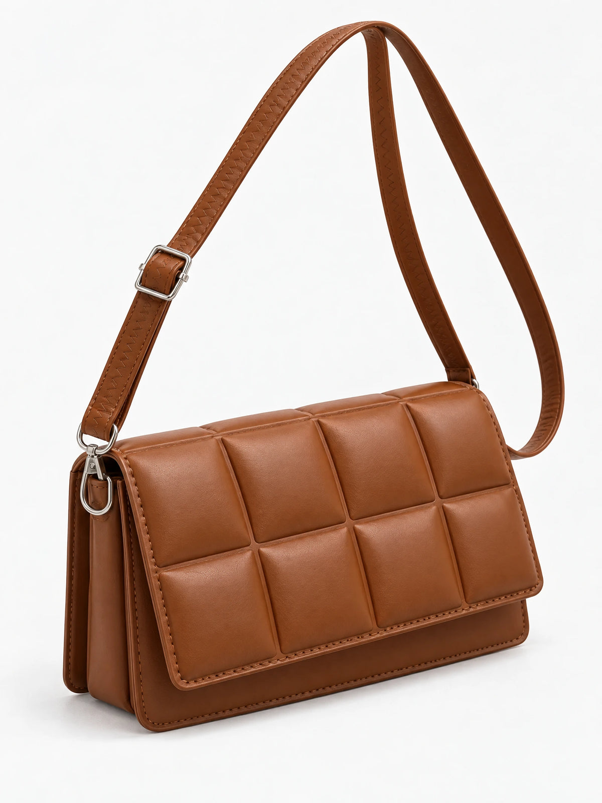 Brown leather cross body bag shown at an angle with a padded grid front flap, adjustable strap, and metal hardware.
