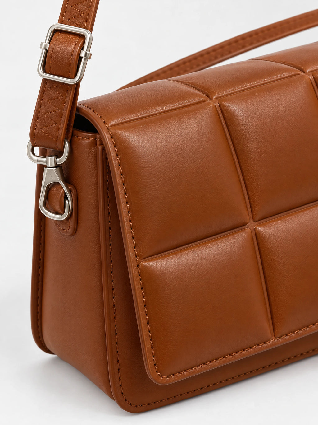 Close-up of the Brown leather cross body bag with padded panel stitching, adjustable strap, and metal swivel clasp.