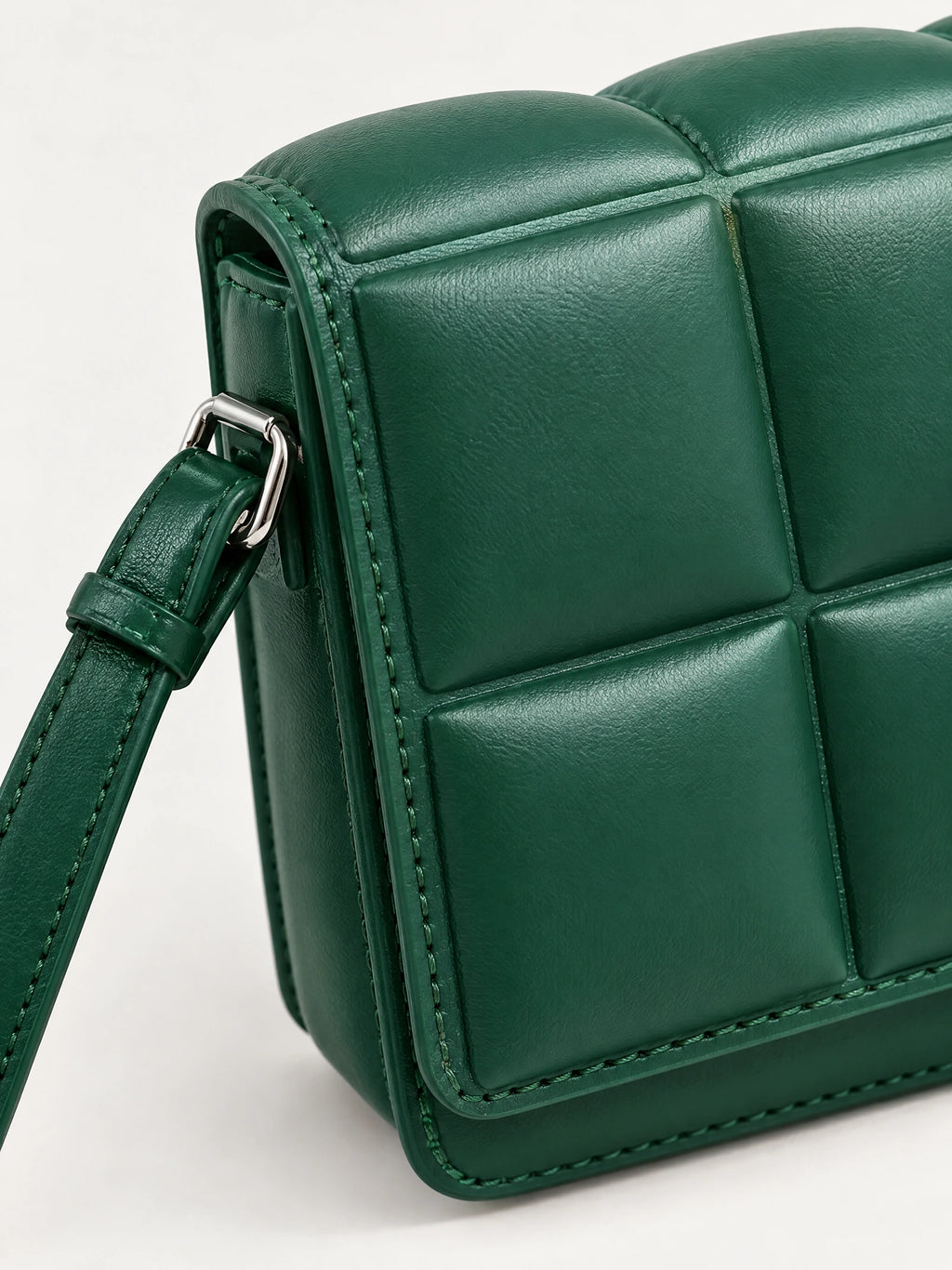 Close-up of a Green leather cross body bag with padded panel stitching and an adjustable strap buckle.
