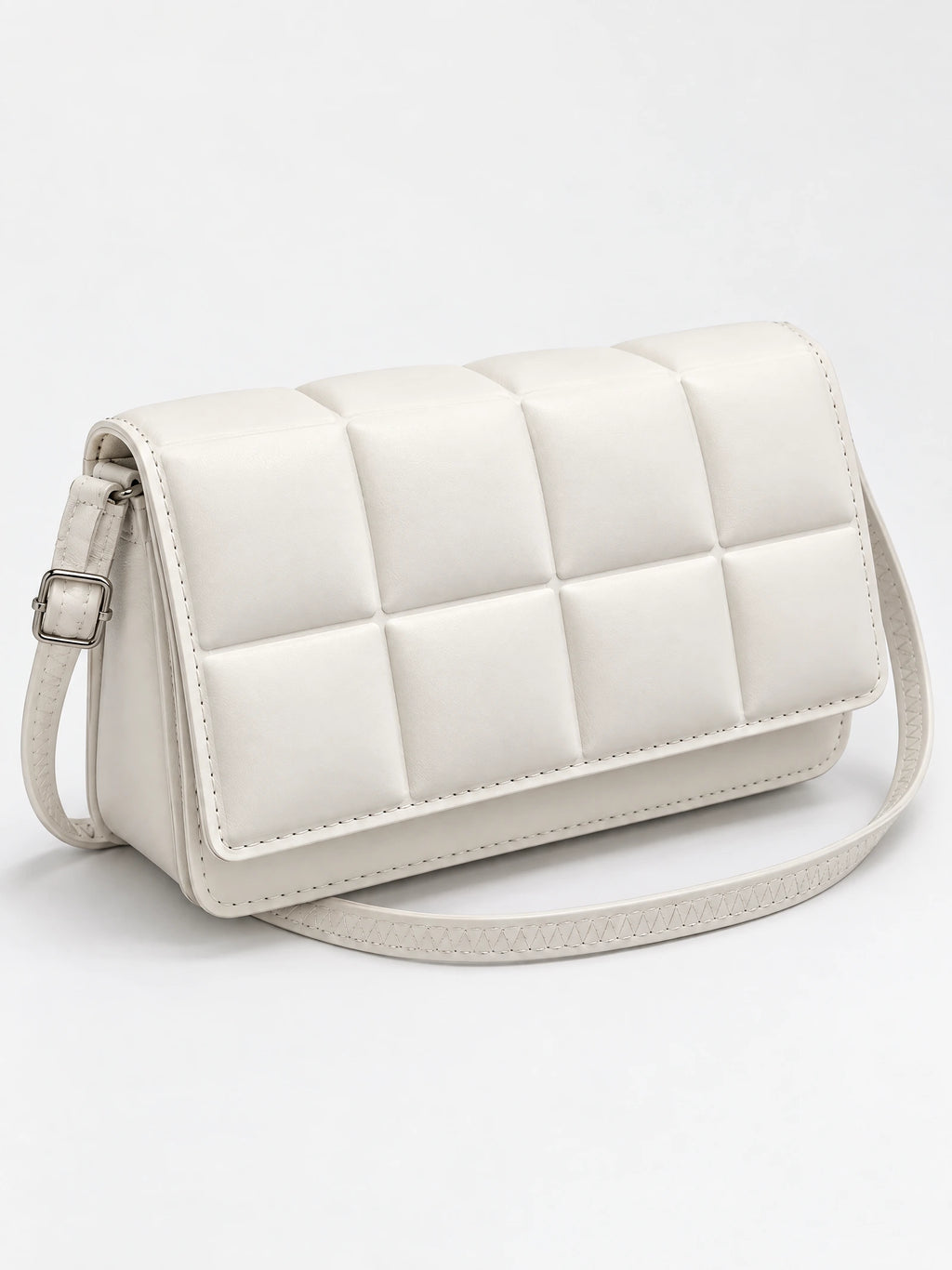 White leather cross body bag shown at an angle with a padded square-panel flap and adjustable buckle strap.