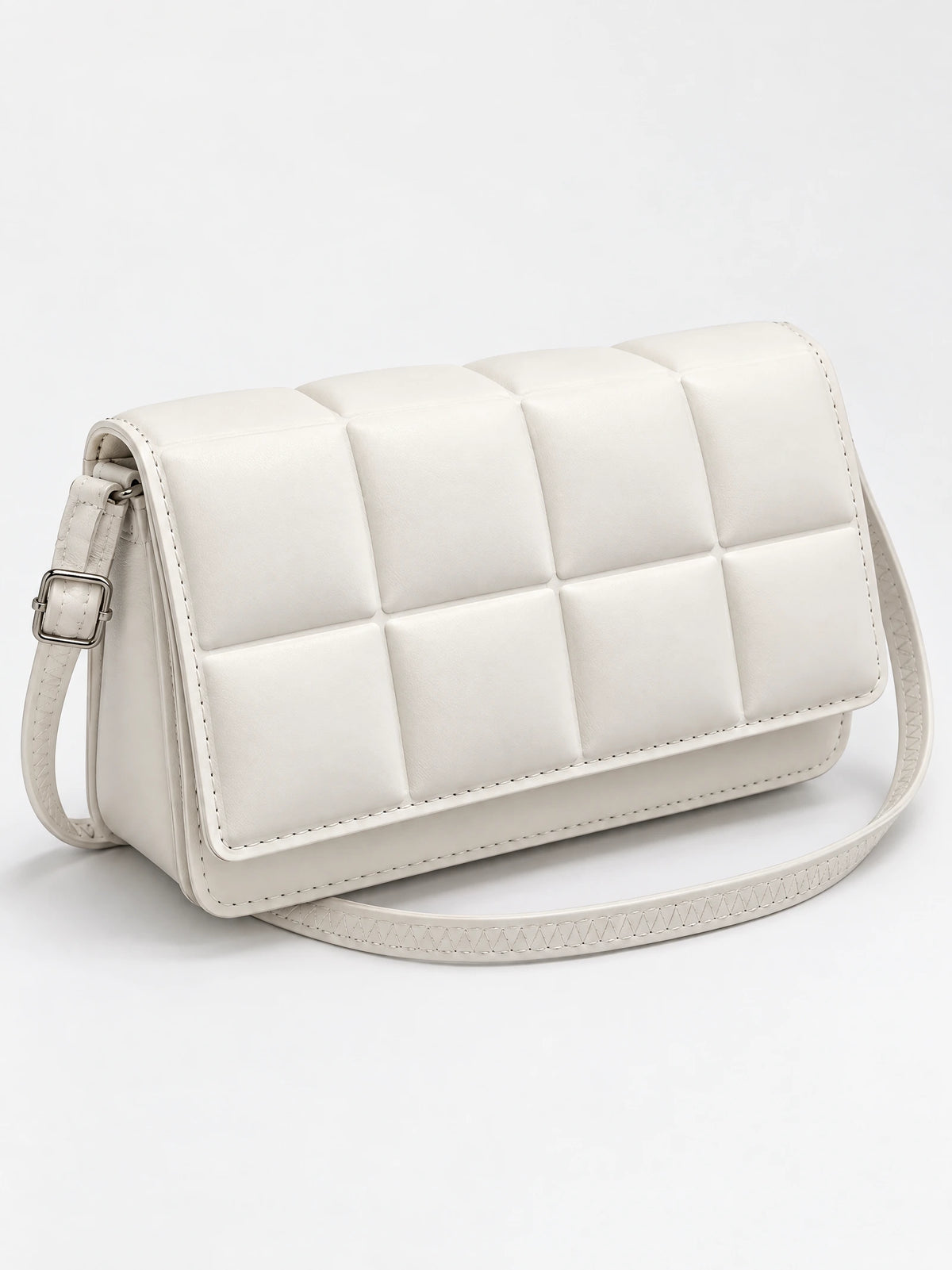 White leather cross body bag shown at an angle with a padded square-panel flap and adjustable buckle strap.