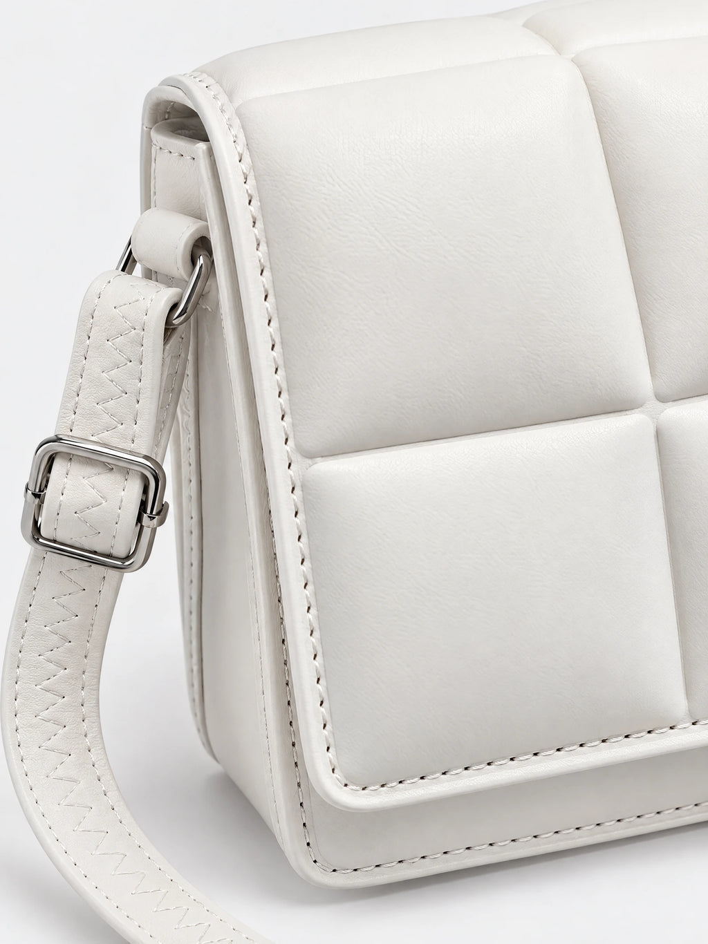 Close-up of the White leather cross body bag showing padded panels, stitched strap, and adjustable metal buckle.
