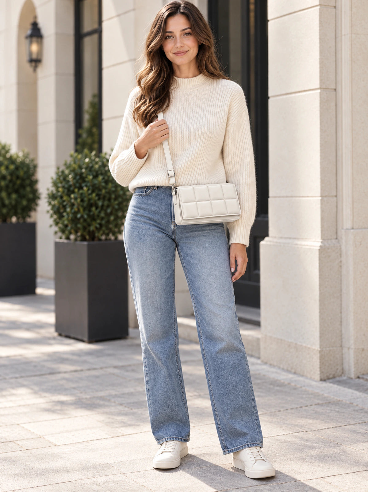 Model wearing a White leather cross body bag with a quilted flap while standing outside a stone-fronted building.