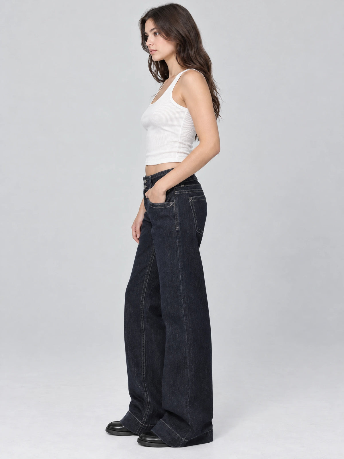 Side studio view of a model wearing Blue Lowe Rise Jeans with a wide-leg fit, visible front pocket, and contrast stitching.