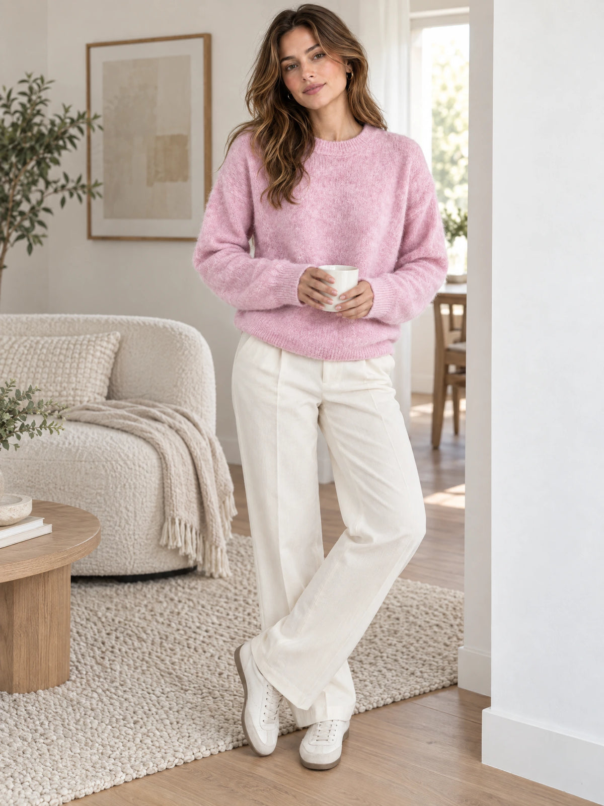 Woman wearing a Pink mohair winter sweater with ribbed trim while holding a mug in a bright living room.