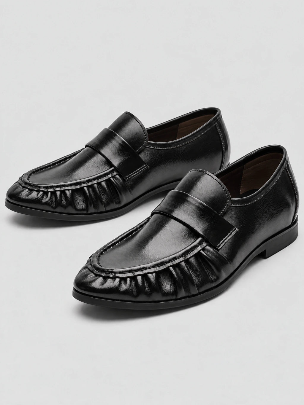 Black ruched leather loafers shown as a pair in a studio product photo, with moc-toe stitching and low flat heels.
