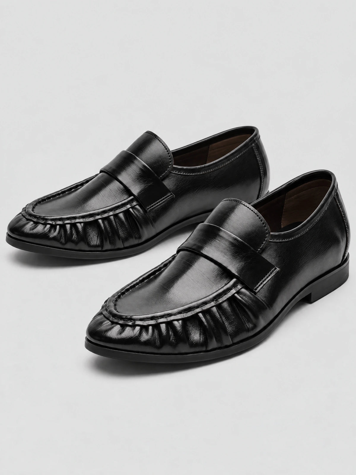 Black ruched leather loafers shown as a pair in a studio product photo, with moc-toe stitching and low flat heels.