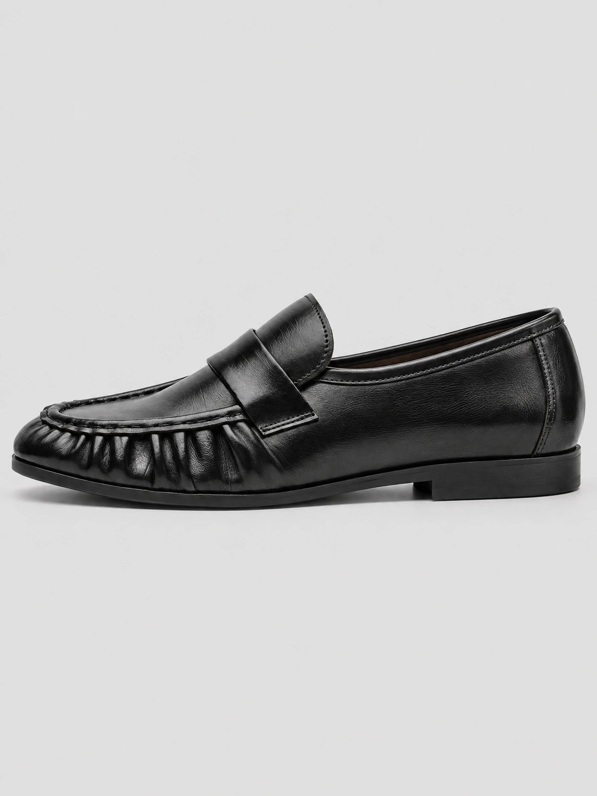 Side view of a Black ruched leather loafer with a round toe, stitched apron, and low flat heel.