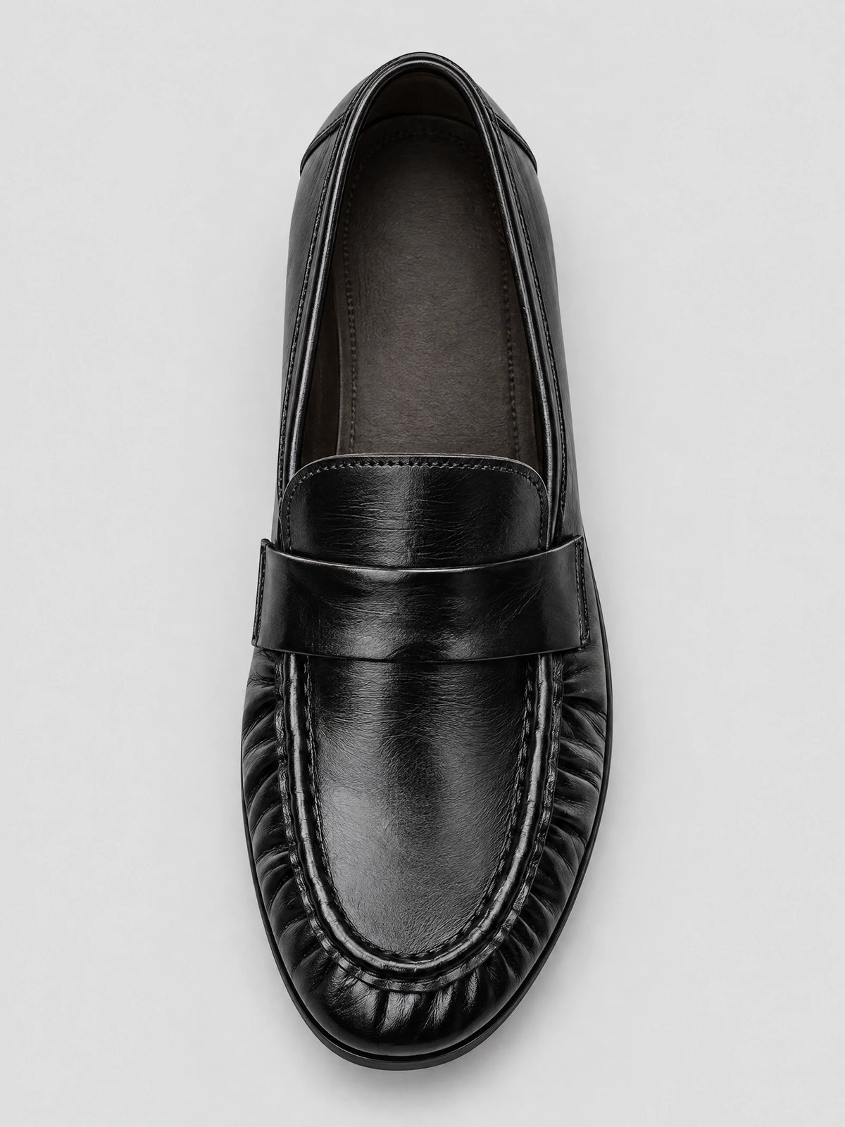 Top-down close-up of a Black ruched leather loafer with a wide vamp strap and gathered stitching around the toe.