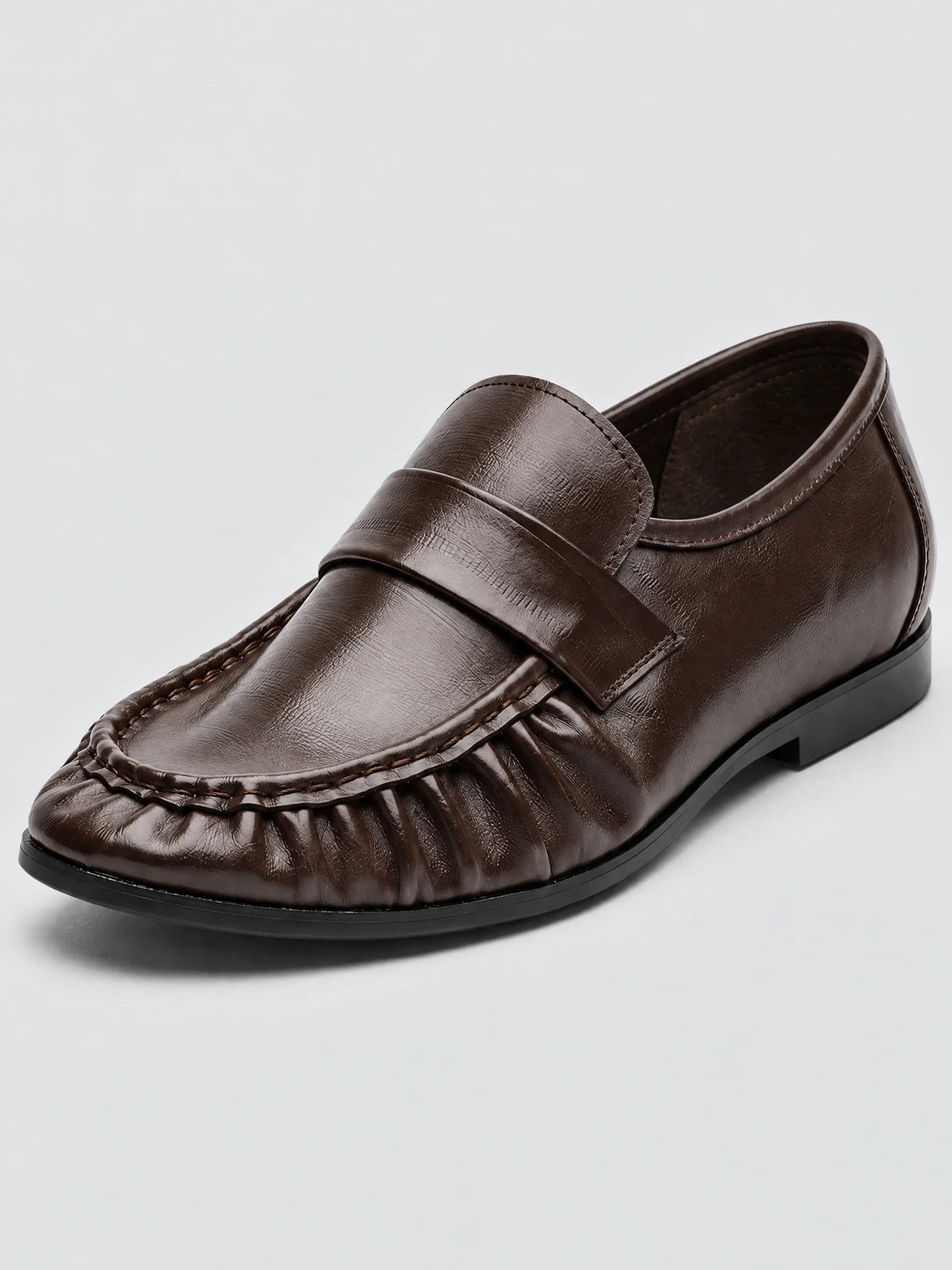 Brown ruched leather loafer in a three-quarter studio close-up, showing the stitched apron toe, vamp strap, and flat sole.