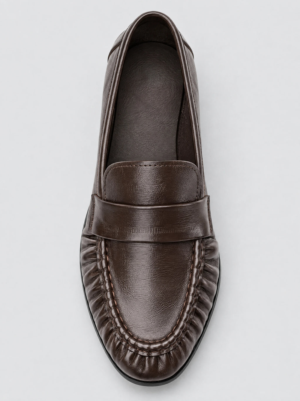 Top-down close-up of a Brown ruched leather loafer with stitched apron detailing and a penny strap.