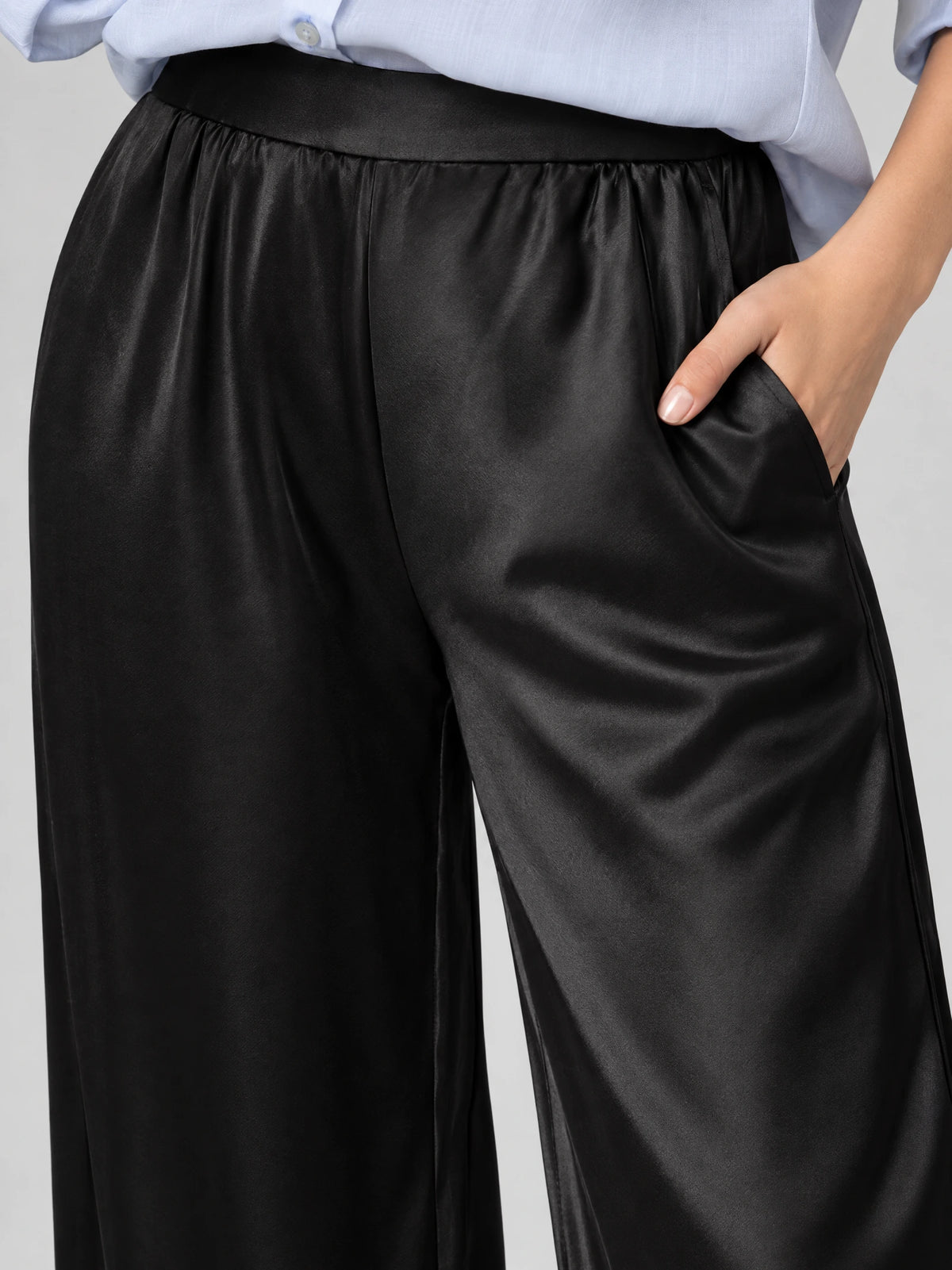 Close-up of Black satin wide leg pants showing the high waistband, gathered front, and side pocket.