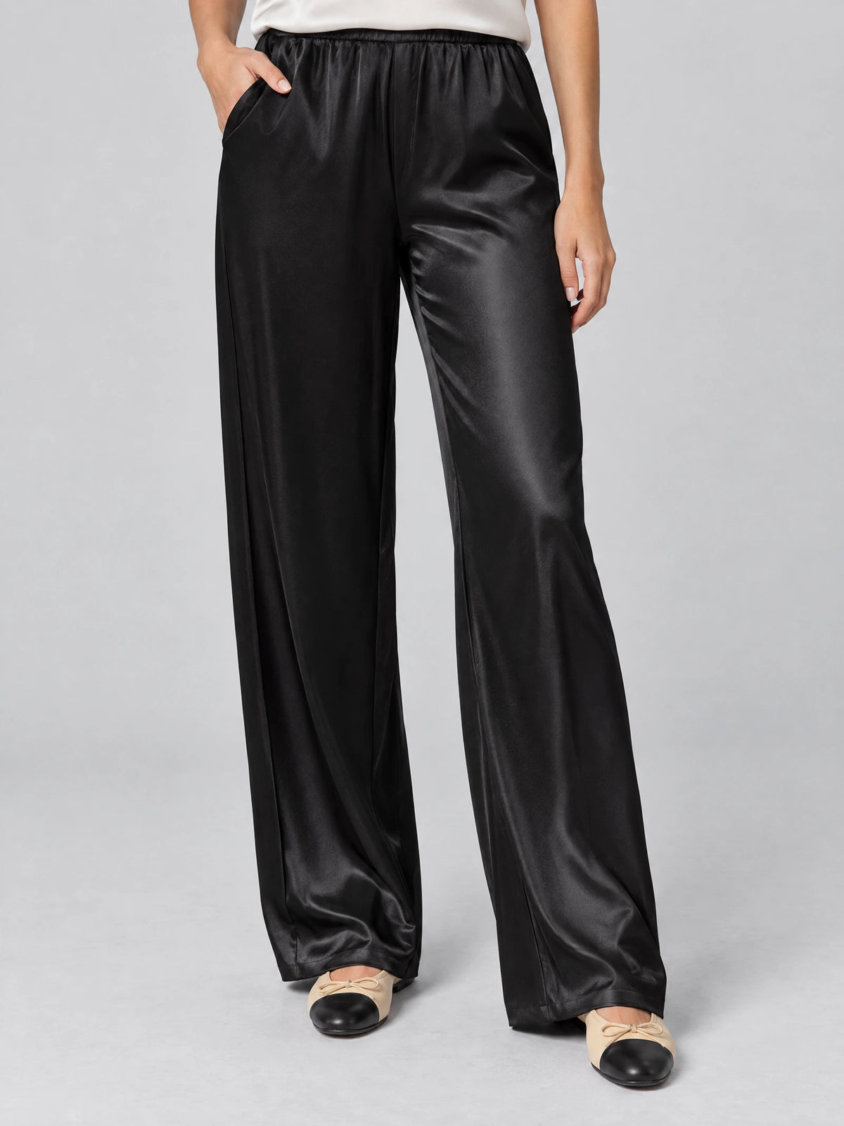 Front studio view of a model wearing Black satin wide leg pants with an elastic high waist and side pockets.