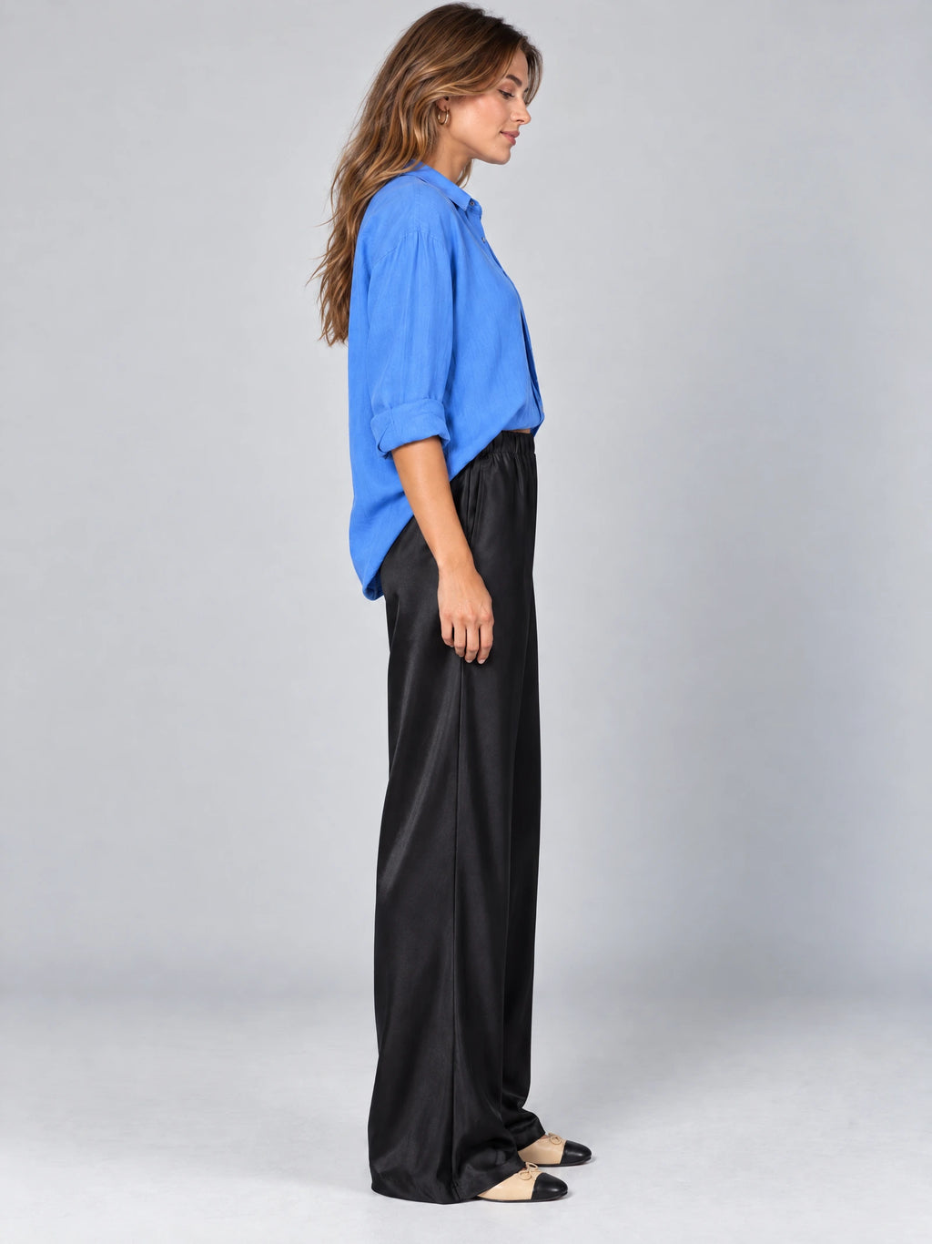 Side studio view of a model wearing Black satin wide leg pants with a high elastic waist.