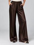 Front studio view of a model wearing Brown satin wide leg pants with a high waistband and side pockets.